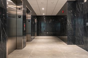 A long hallway with marble floors and walls and elevators on the side